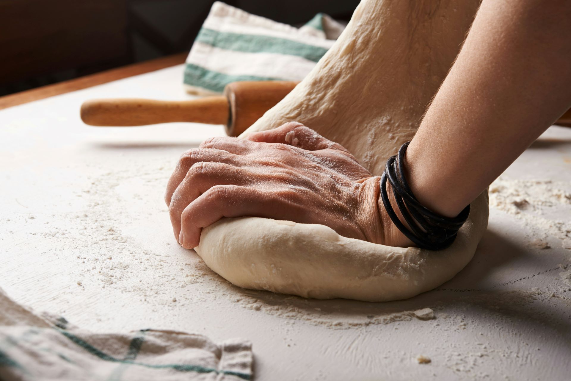 Ein Teig wird von Hand geknetet, um eine perfekte Basis für Pizza zuzubereiten, mit Nudelholz und Mehl im Hintergrund