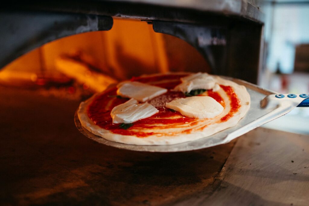 Pizza auf einem Pizzaschieber wird in einen heißen Backofen mit Pizzastein geschoben, ideal für einen knusprigen Boden