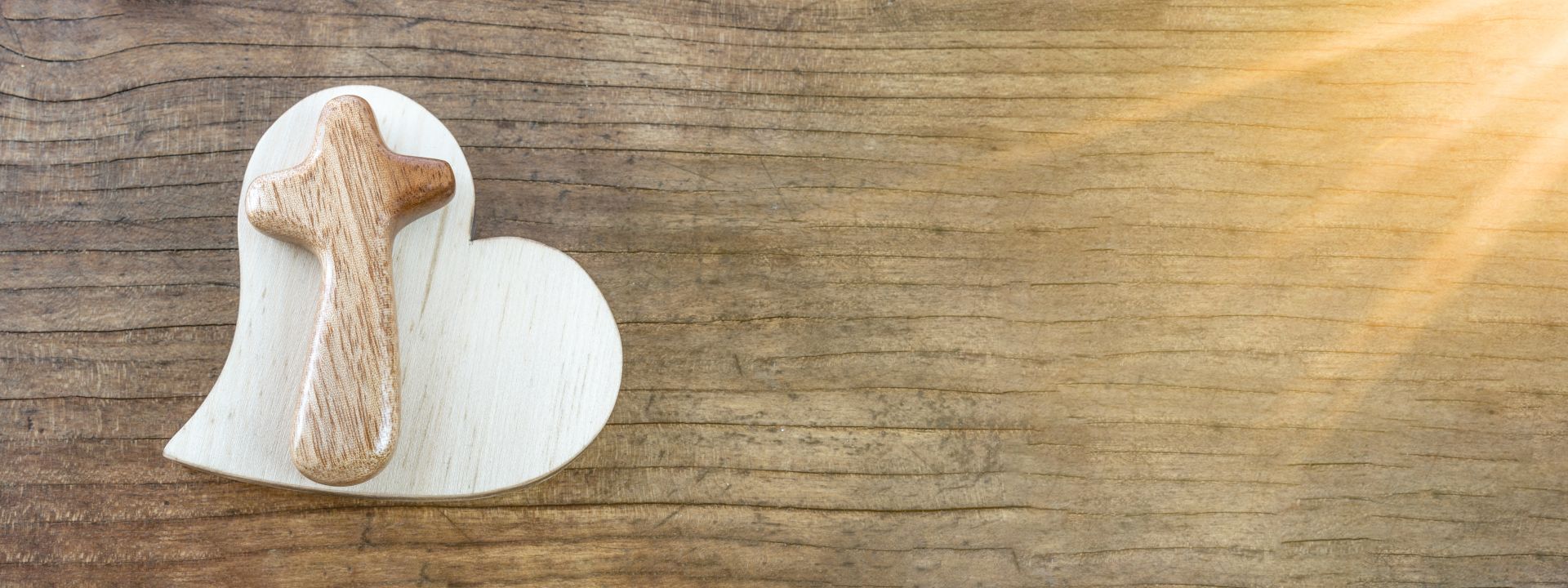 Herzförmiges Holzbrett mit geschnitztem Holzkreuz, auf natürlicher Holzoberfläche mit Sonnenstrahlen