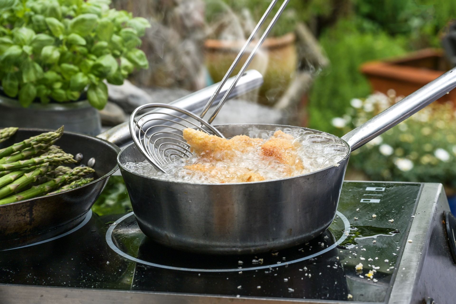 Induktionskochfeld in der Außenküche mit frischem Gemüse und heißem Öl.