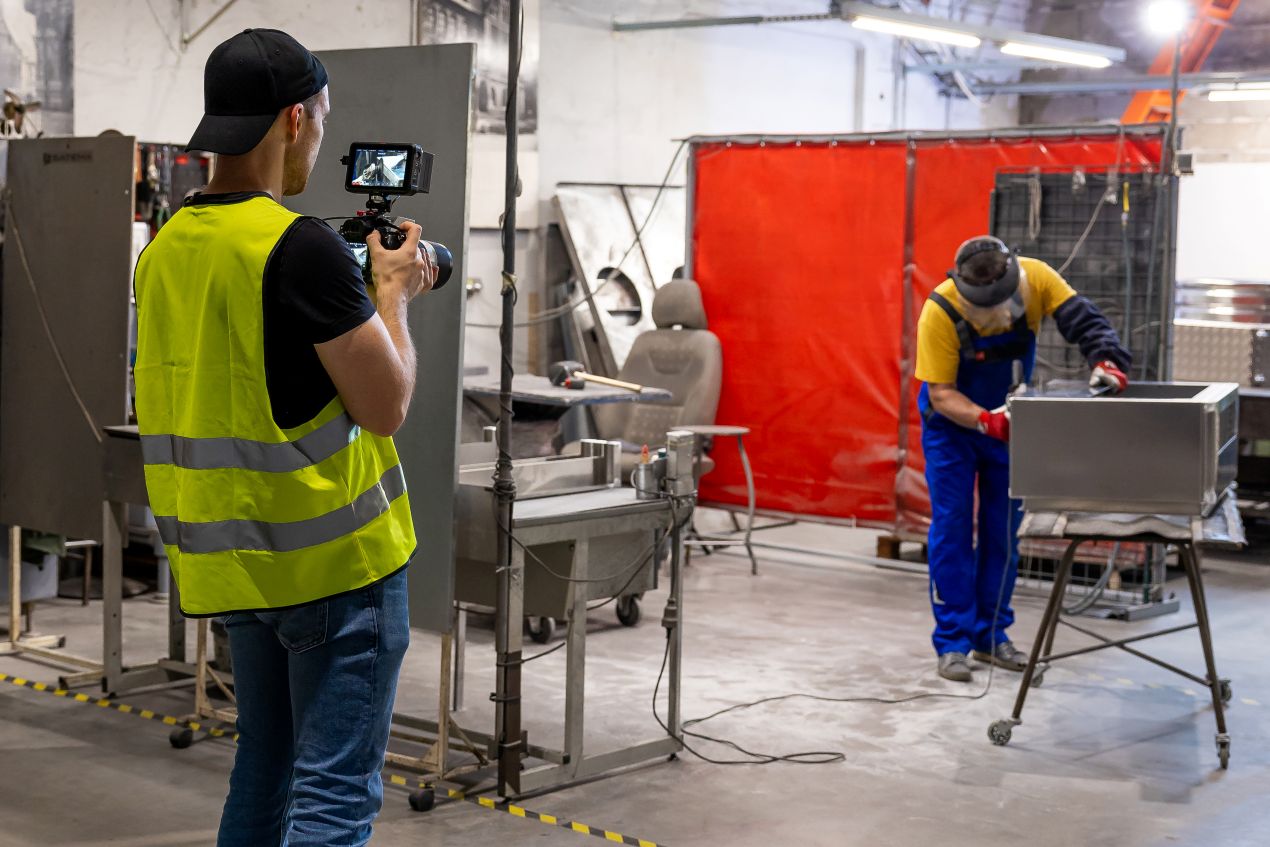 Videoproduktion Köln in einer Fabrik: Ein Kameramann filmt einen Arbeiter bei der Metallbearbeitung – authentische Einblicke in den Arbeitsalltag.